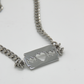 A commemorative necklace celebrating the twenty fifth anniversary of Razorblade Romance. A thick stainless steel chain with a razor blade pendant at the middle. 